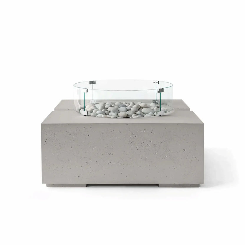 HPC Fire Hearth Products Controls Dekko GFRC Concrete Bravo 32 x 32 Fire Pit in Sandstone finish with Ivory Stone fire media and a clear tempered glass wind guard. The warm beige concrete texture pairs naturally with the light decorative stones, creating an inviting outdoor fire feature with a contemporary square design and premium architectural styling.