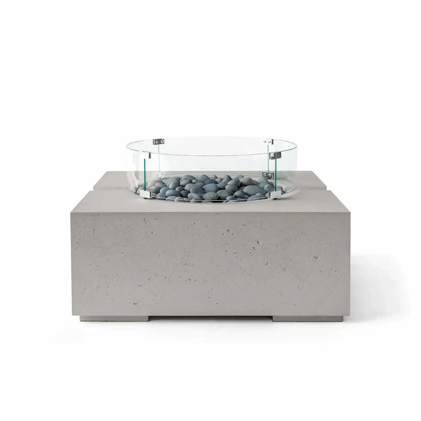 HPC Fire Hearth Products Controls Dekko GFRC Concrete Bravo 32 x 32 Fire Pit in Sandstone finish with Slate Stone fire media and a clear tempered glass wind guard. The combination of warm beige concrete and smooth gray stones delivers a refined contemporary look, while the square fire pit design and textured GFRC construction provide lasting outdoor style.