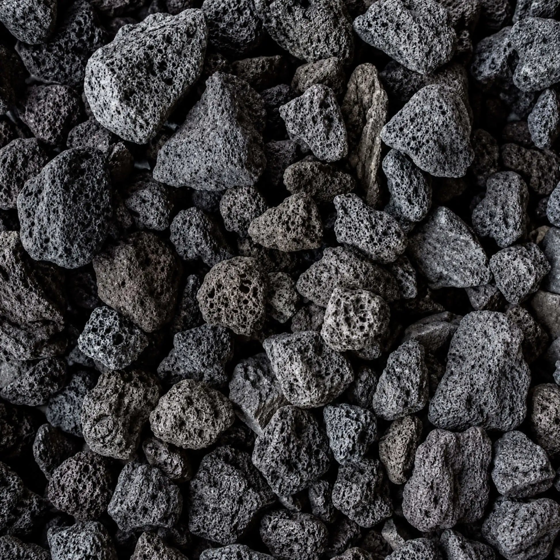 Detailed close-up of HPC Fire Hearth Products Dekko GFRC Concrete Fire Pit Media Lava Rock, showcasing porous volcanic stones with rugged textures and natural black, charcoal, and dark gray coloration. The lightweight lava rock media features irregular shapes and highly textured surfaces designed to enhance flame presentation in outdoor gas fire pits, fire bowls, and custom fire features.