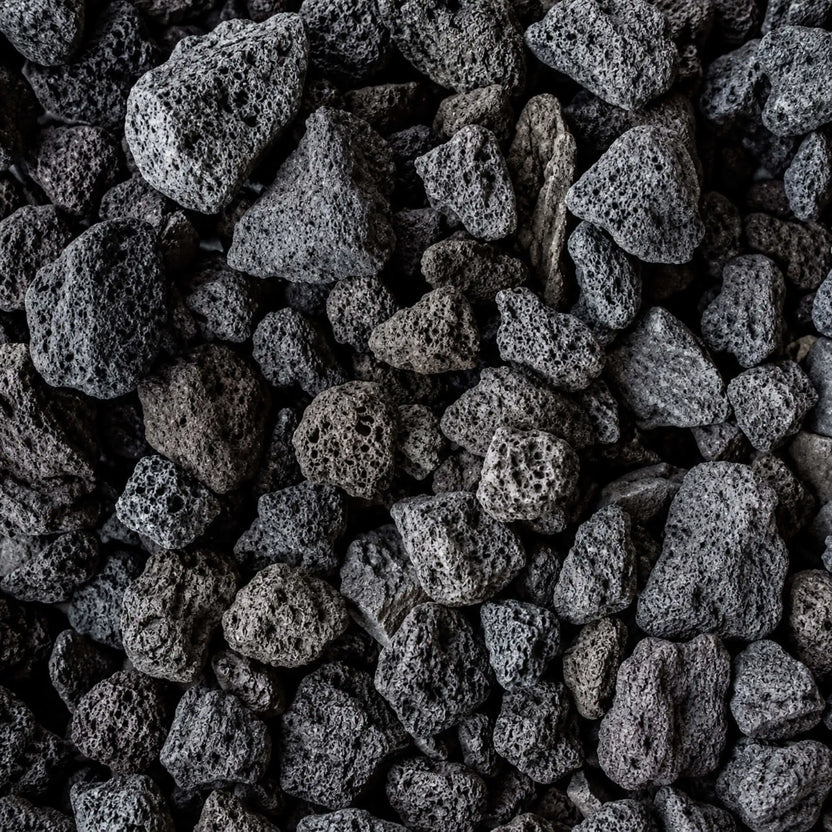 Detailed close-up of HPC Fire Hearth Products Dekko GFRC Concrete Fire Pit Media Lava Rock, showcasing porous volcanic stones with rugged textures and natural black, charcoal, and dark gray coloration. The lightweight lava rock media features irregular shapes and highly textured surfaces designed to enhance flame presentation in outdoor gas fire pits, fire bowls, and custom fire features.
