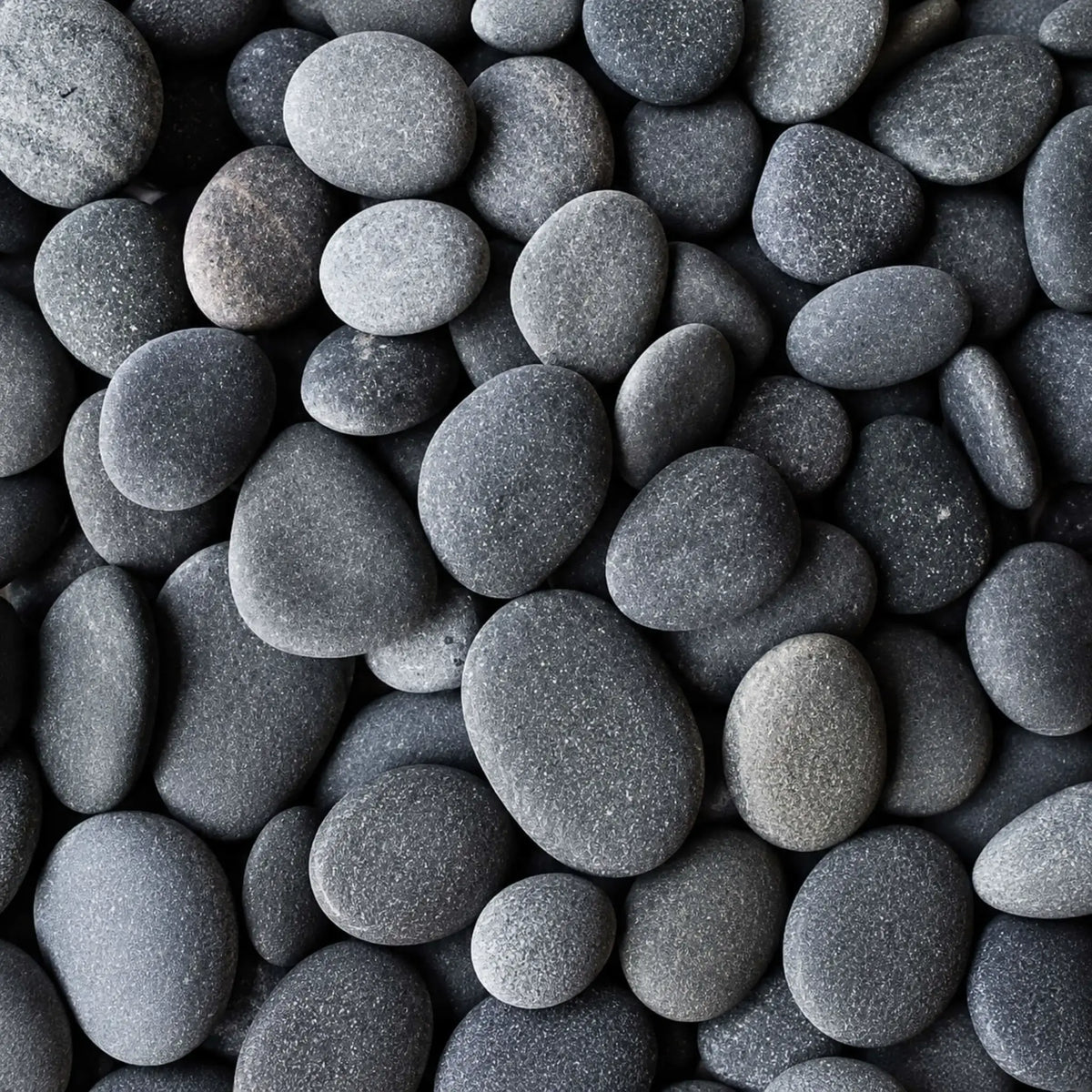Macro image of HPC Fire Hearth Products Dekko GFRC Concrete Fire Pit Media Slate Beach Stone, displaying smooth rounded beach stones in rich slate gray and charcoal tones. The naturally shaped decorative stones feature a matte finish and varied sizes, creating a modern, sophisticated fire pit media option for outdoor gas fire tables, fire bowls, and landscape fire feature installations.