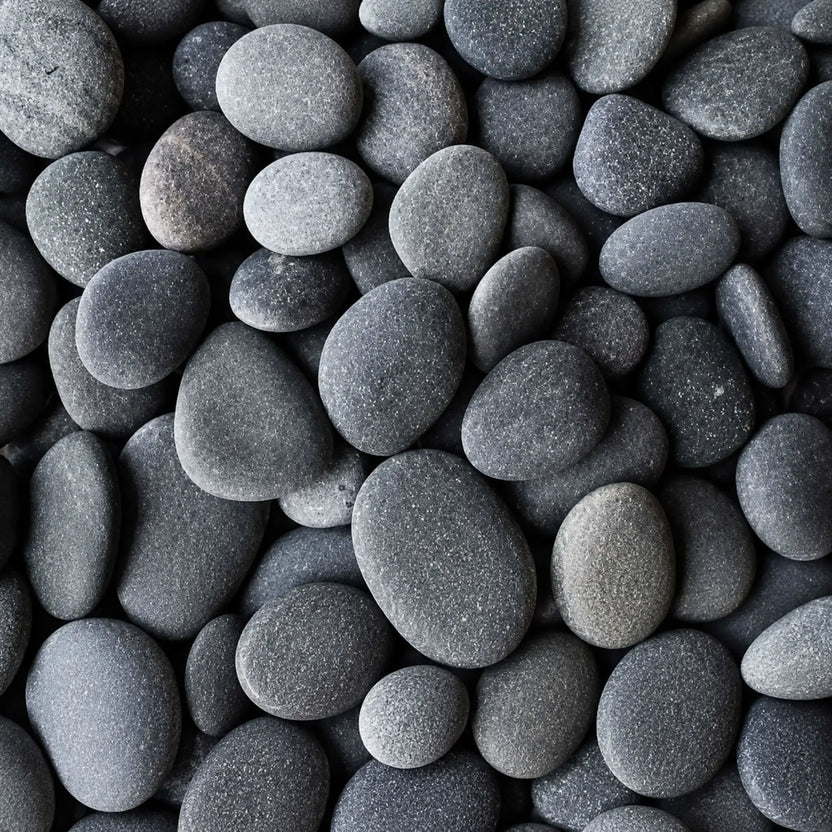 Macro image of HPC Fire Hearth Products Dekko GFRC Concrete Fire Pit Media Slate Beach Stone, displaying smooth rounded beach stones in rich slate gray and charcoal tones. The naturally shaped decorative stones feature a matte finish and varied sizes, creating a modern, sophisticated fire pit media option for outdoor gas fire tables, fire bowls, and landscape fire feature installations.