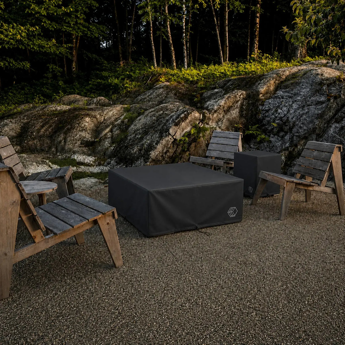 HPC Fire Hearth Products Controls Dekko GFRC Concrete Propane Tank Cover Weather Cover displayed in an outdoor gathering space surrounded by rustic wooden Adirondack chairs and natural rock landscaping. The black weather cover protects a square Dekko propane tank enclosure while blending into the backyard environment, showcasing its ability to shield outdoor fire pit accessories and propane storage components from weather, debris, and seasonal exposure.