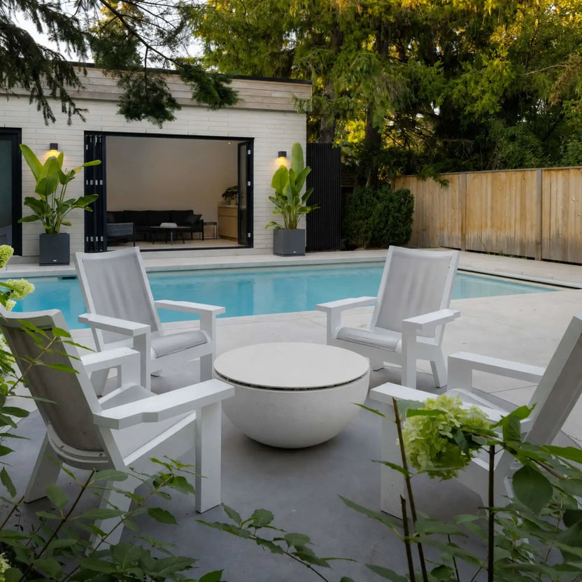 HPC Fire Hearth Products Controls Dekko GFRC Concrete Serenade 32 Fire Pit Table Top Lid used as a central outdoor coffee table in a backyard seating area. Surrounded by white Adirondack-style chairs near a swimming pool and pool house, the covered fire pit creates a clean and functional gathering space. The image highlights the versatility of the Serenade 32 tabletop lid in residential outdoor living environments.