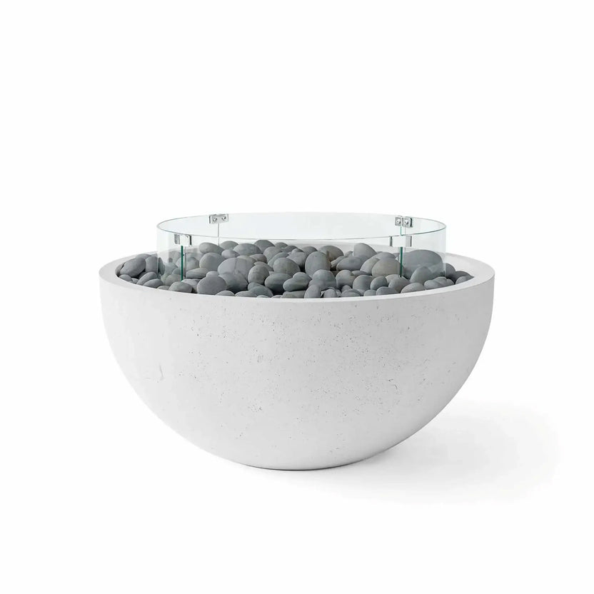 HPC Fire Hearth Products Controls Dekko GFRC Concrete Serenade 40 Fire Pit finished in Ash with decorative slate stone fire media and a clear tempered glass wind guard. The contemporary concrete fire bowl features smooth rounded edges, durable GFRC construction, gray polished stones surrounding the burner area, and a circular glass windscreen, creating a refined focal point for modern patios and outdoor entertaining areas.
