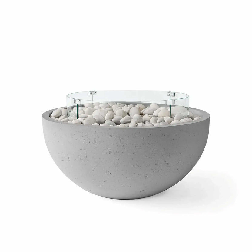HPC Fire Hearth Products Controls Dekko GFRC Concrete Serenade 40 Fire Pit in Charcoal finish featuring ivory stone fire media and a tempered glass wind guard. The sleek round fire pit combines a dark charcoal concrete bowl with bright white decorative stones and a circular glass flame barrier, offering a striking contrast that complements contemporary outdoor seating areas and luxury landscape designs.