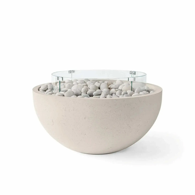 HPC Fire Hearth Products Controls Dekko GFRC Concrete Serenade 40 Fire Pit in Clay finish featuring ivory stone fire media and a clear tempered glass wind guard. The warm clay-colored concrete bowl is filled with decorative white river stones and surrounded by a circular glass flame barrier, creating a sophisticated outdoor fire feature suited for contemporary and transitional patio environments.