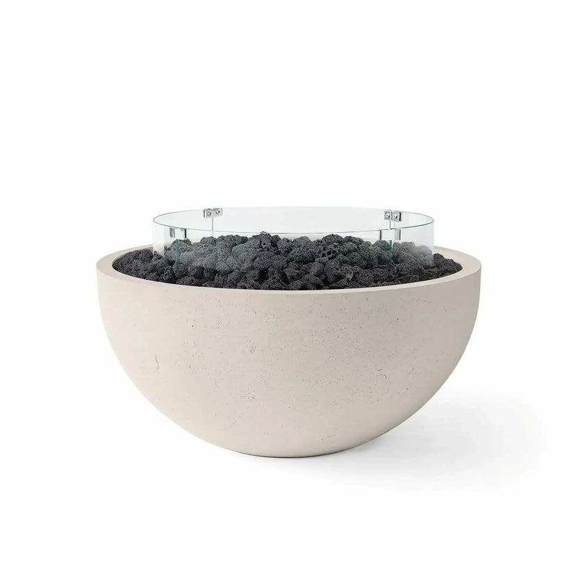 HPC Fire Hearth Products Controls Dekko GFRC Concrete Serenade 40 Fire Pit in Clay finish with black lava rock fire media and a tempered glass wind guard. This modern GFRC concrete fire bowl combines a soft beige clay tone with textured volcanic lava rock and a circular glass windscreen, delivering a bold contrast and stylish focal point for outdoor living and entertainment spaces.