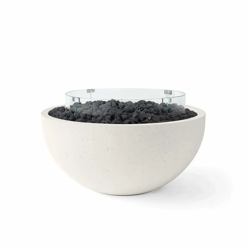 HPC Fire Hearth Products Controls Dekko GFRC Concrete Serenade 40 Fire Pit in Limestone finish featuring black lava rock fire media and a clear tempered glass wind guard. This contemporary round GFRC concrete fire bowl combines a soft limestone-colored exterior with rugged volcanic lava rock and a circular glass flame barrier, creating a clean, modern outdoor fire feature ideal for luxury patios, poolside spaces, and upscale backyard entertaining areas.