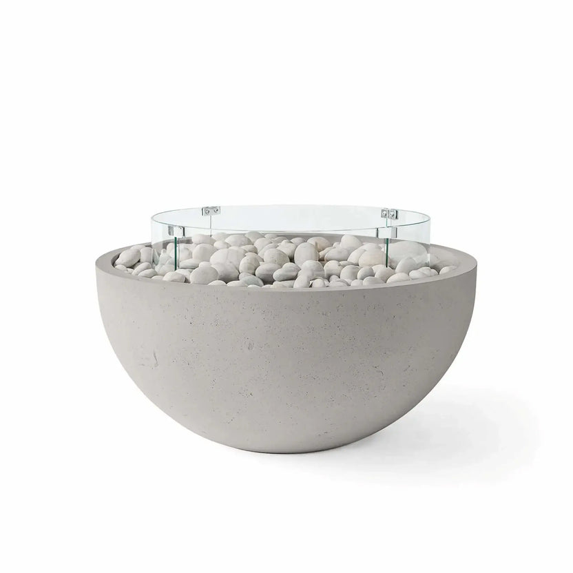 HPC Fire Hearth Products Controls Dekko GFRC Concrete Serenade 40 Fire Pit in Sandstone finish with ivory stone fire media and a tempered glass wind guard. The warm sandstone-colored GFRC concrete bowl is accented by smooth white river stones and a circular glass flame barrier, creating a welcoming and sophisticated outdoor centerpiece perfect for patios, courtyards, and luxury residential landscapes.