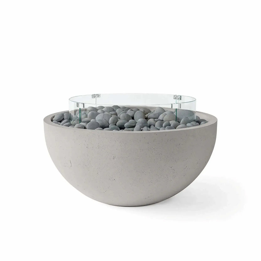 HPC Fire Hearth Products Controls Dekko GFRC Concrete Serenade 40 Fire Pit in Sandstone finish with slate stone fire media and a tempered glass wind guard. Featuring a textured GFRC concrete bowl, smooth gray decorative stones, and a circular glass flame barrier, this contemporary outdoor fire pit offers a clean architectural look suited for upscale patios, terraces, and backyard retreats.