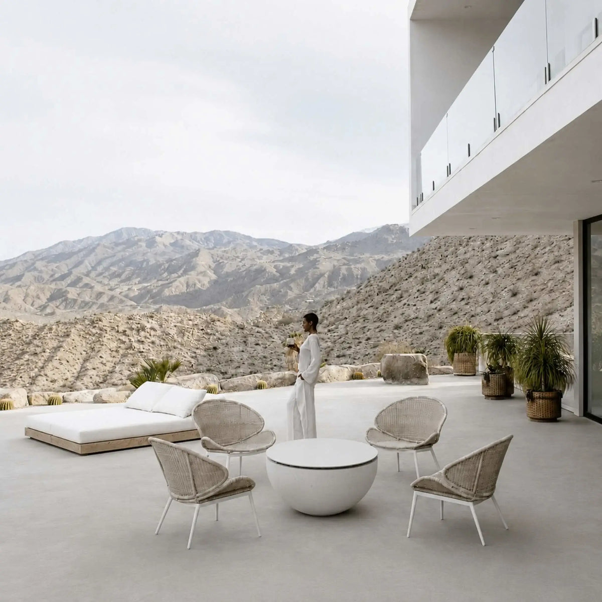 HPC Fire Hearth Products Controls Dekko GFRC Concrete Serenade 40 Fire Pit Table Top Lid displayed on a spacious contemporary terrace with panoramic mountain views. Surrounded by woven lounge chairs, the covered Serenade 40 fire pit acts as a functional centerpiece and outdoor coffee table. The round tabletop lid protects the burner area while preserving the clean, minimalist aesthetic of the luxury outdoor setting.