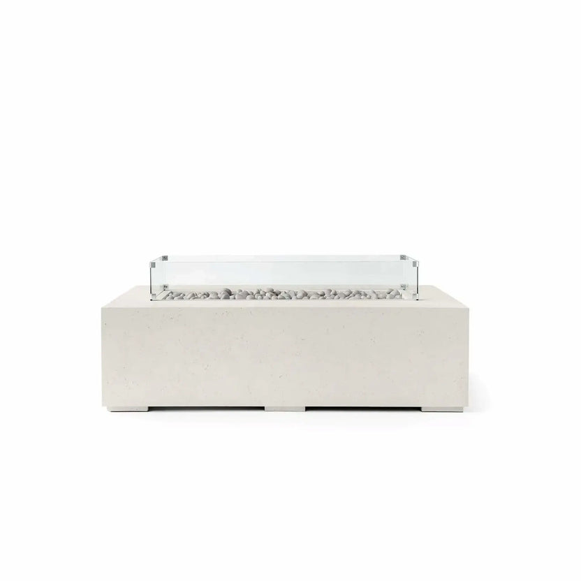 HPC Fire Hearth Products Controls Dekko GFRC Concrete Sonoma 56 x 30 Fire Pit in Limestone finish featuring Ivory Stone media and a tempered glass wind guard. The light limestone-colored concrete body complements the smooth ivory stones arranged across the recessed linear burner channel, while the transparent wind guard helps shield flames from wind. This contemporary outdoor fire pit offers a clean architectural appearance that fits seamlessly into modern patios, poolside retreats, and upscale outdoor ente