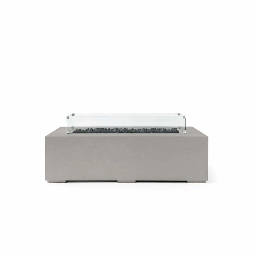 HPC Fire Hearth Products Controls Dekko GFRC Concrete Sonoma 56 x 30 Fire Pit in Sandstone finish featuring black Lava Rock media and a tempered glass wind guard. This rectangular outdoor fire pit combines a warm sandstone GFRC concrete body with dark volcanic lava rock inside the recessed burner channel, creating strong visual contrast. The transparent glass wind guard completes the sophisticated design while helping protect flames from outdoor breezes.