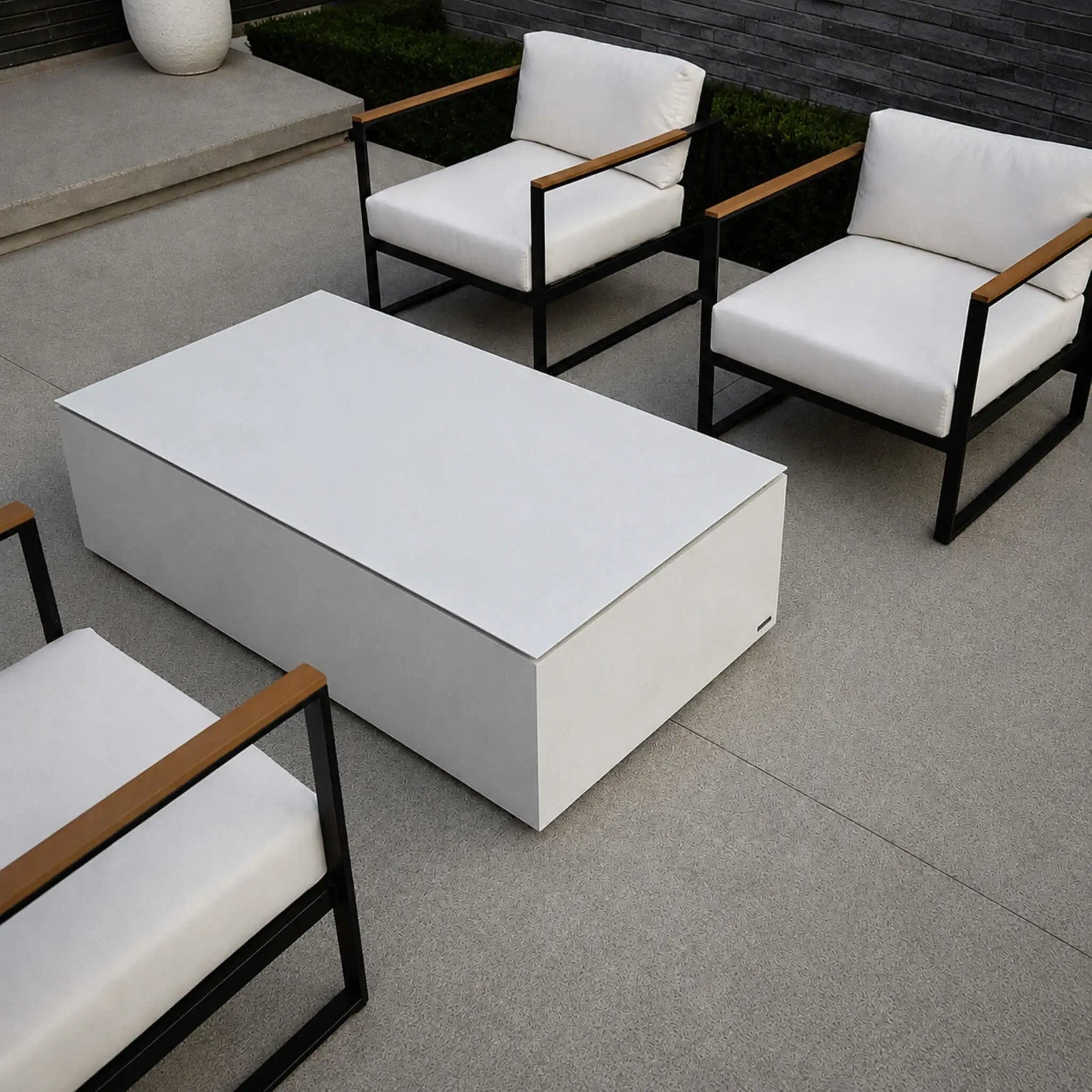 HPC Fire Hearth Products Controls Dekko GFRC Concrete Sonoma 56 x 30 Fire Pit Table Top Lid Lifestyle 2 image showing a top-down perspective of the covered fire pit used as an outdoor coffee table. The sleek tabletop lid creates a large functional surface positioned between contemporary lounge chairs with white cushions and black metal frames. The image demonstrates how the Sonoma fire pit seamlessly integrates into modern patio furniture arrangements while maximizing usability.
