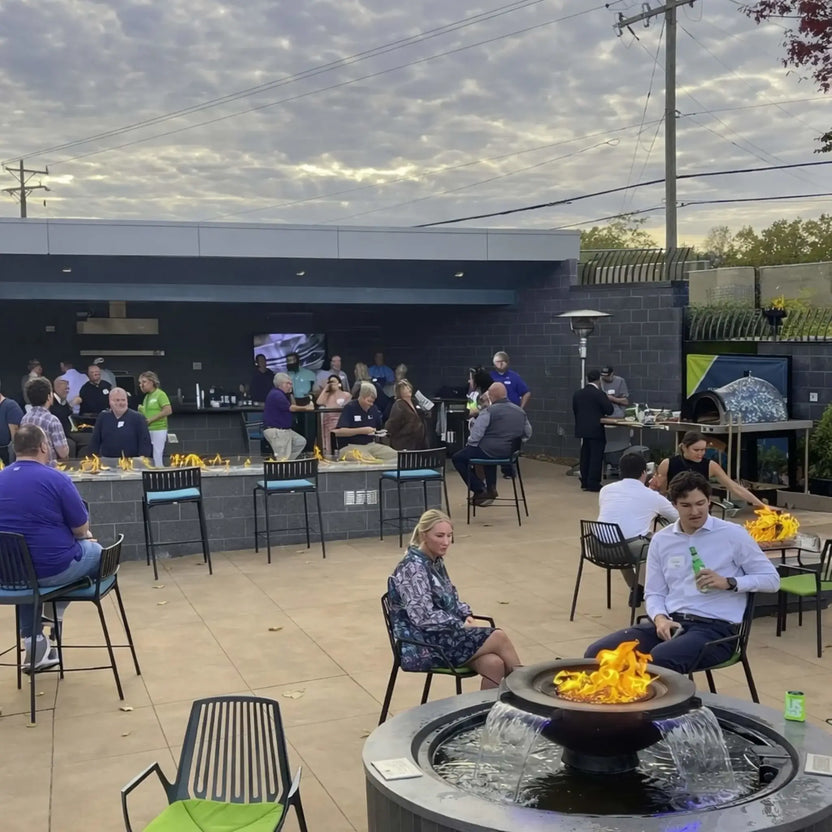 Wide view of a modern outdoor entertainment space featuring multiple fire elements, including the HPC Fire Evolution 360 fire and water feature in the foreground. Guests sit and socialize around fire tables and a central bar, showcasing the ambiance and versatility of integrated fire and water features in commercial settings.