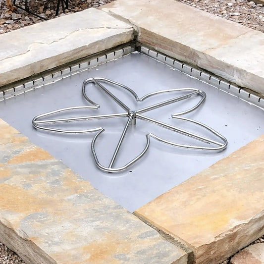 Square outdoor fire pit enclosure built with natural stone blocks featuring a stainless steel flex form installation collar fitted along the inner perimeter. A custom multi-petal gas burner sits centered on a smooth metal base, showing how the collar supports proper insert placement within a finished fire pit structure.