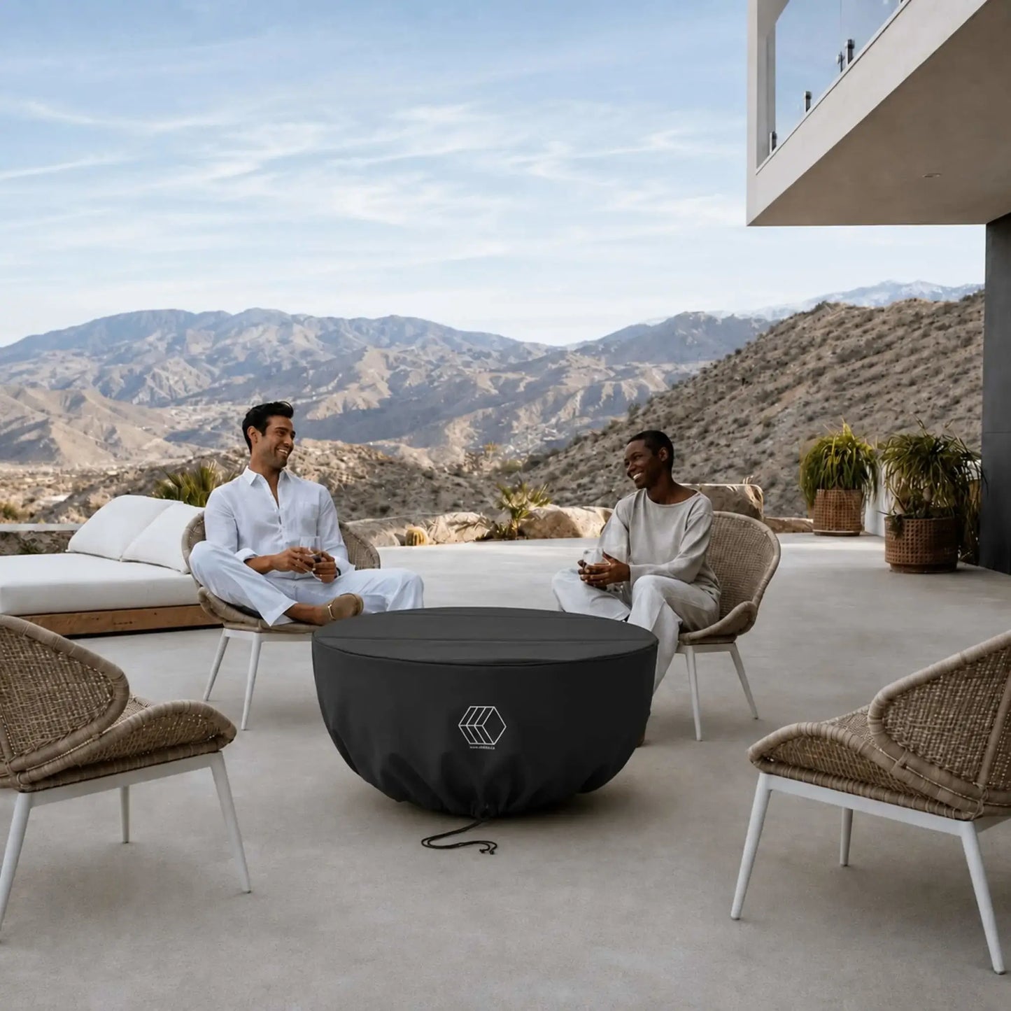 HPC Fire Hearth Products Controls GFRC Concrete Serenade 40 Weather Cover featured on a covered fire pit at a modern outdoor living space with panoramic mountain views. Two people relax in surrounding lounge chairs while the black weather cover securely protects the Serenade 40 fire pit between uses. The fitted cover includes a drawstring closure and durable construction, helping preserve the fire pit’s finish and internal components from outdoor exposure.