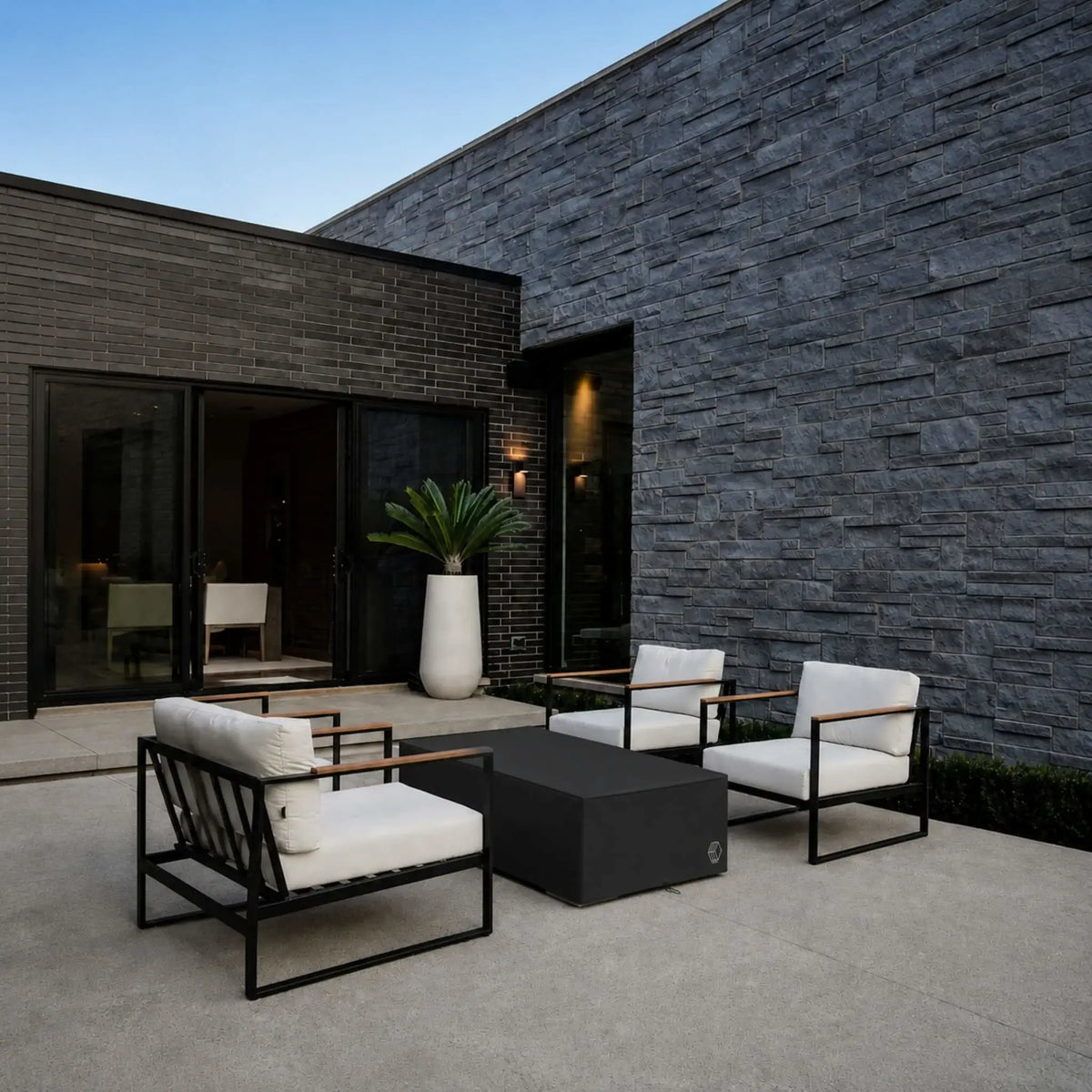 HPC Fire Hearth Products Controls GFRC Concrete Sonoma 56 x 30 Weather Cover Lifestyle 3 image showing the covered Sonoma fire pit integrated into a contemporary courtyard patio. The black protective cover complements the modern outdoor furniture and architectural stone walls while safeguarding the fire feature from weather and debris. This lifestyle scene demonstrates how the cover maintains a clean, polished look when the fire pit is not in use.
