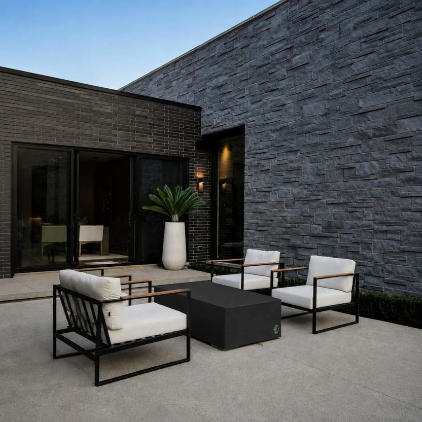 HPC Fire Hearth Products Controls GFRC Concrete Sonoma 56 x 30 Weather Cover Lifestyle 3 image showing the covered Sonoma fire pit integrated into a contemporary courtyard patio. The black protective cover complements the modern outdoor furniture and architectural stone walls while safeguarding the fire feature from weather and debris. This lifestyle scene demonstrates how the cover maintains a clean, polished look when the fire pit is not in use.
