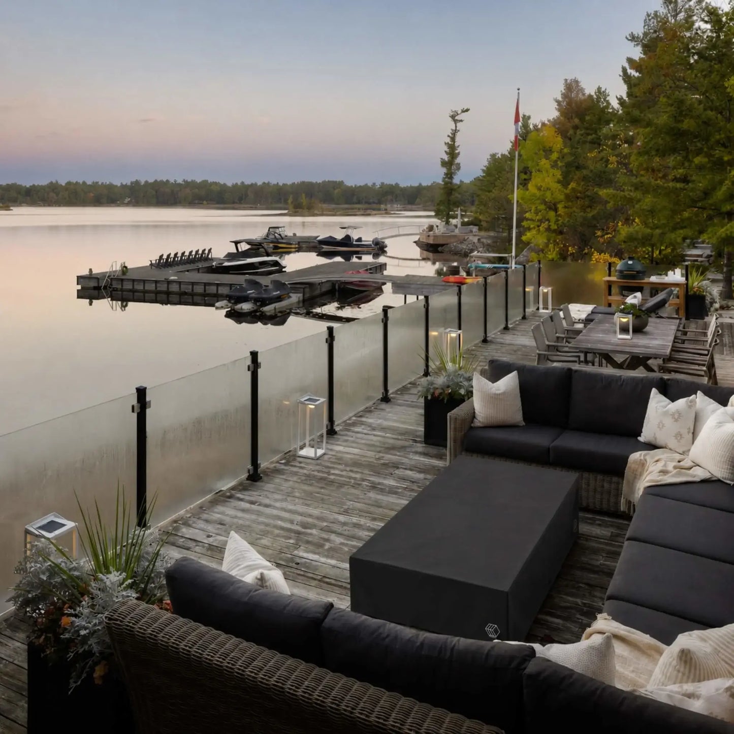 HPC Fire & Hearth Products Controls GFRC Concrete Sonoma 72 x 33 Weather Cover showcased on a waterfront deck overlooking a calm lake and private dock. The black protective cover fits securely over the rectangular Sonoma fire pit table positioned between sectional outdoor seating. With exposure to changing weather conditions near the water, the durable cover highlights its role in protecting outdoor fire pit equipment while preserving a clean and sophisticated entertaining space.