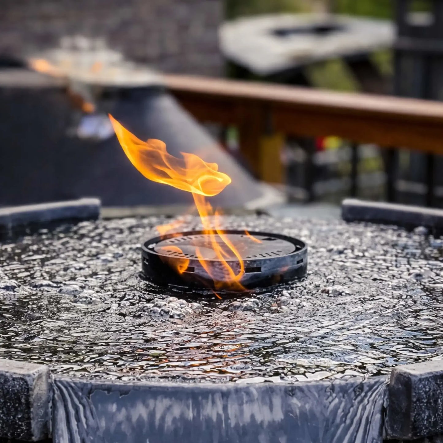 Close-up view of HPC Fire Hearth Products Controls H2O n fire fire water feature burner with a single flame rising above bubbling water. The textured water surface and circular burner design highlight the unique fire-on-water effect used in this award-winning outdoor feature.