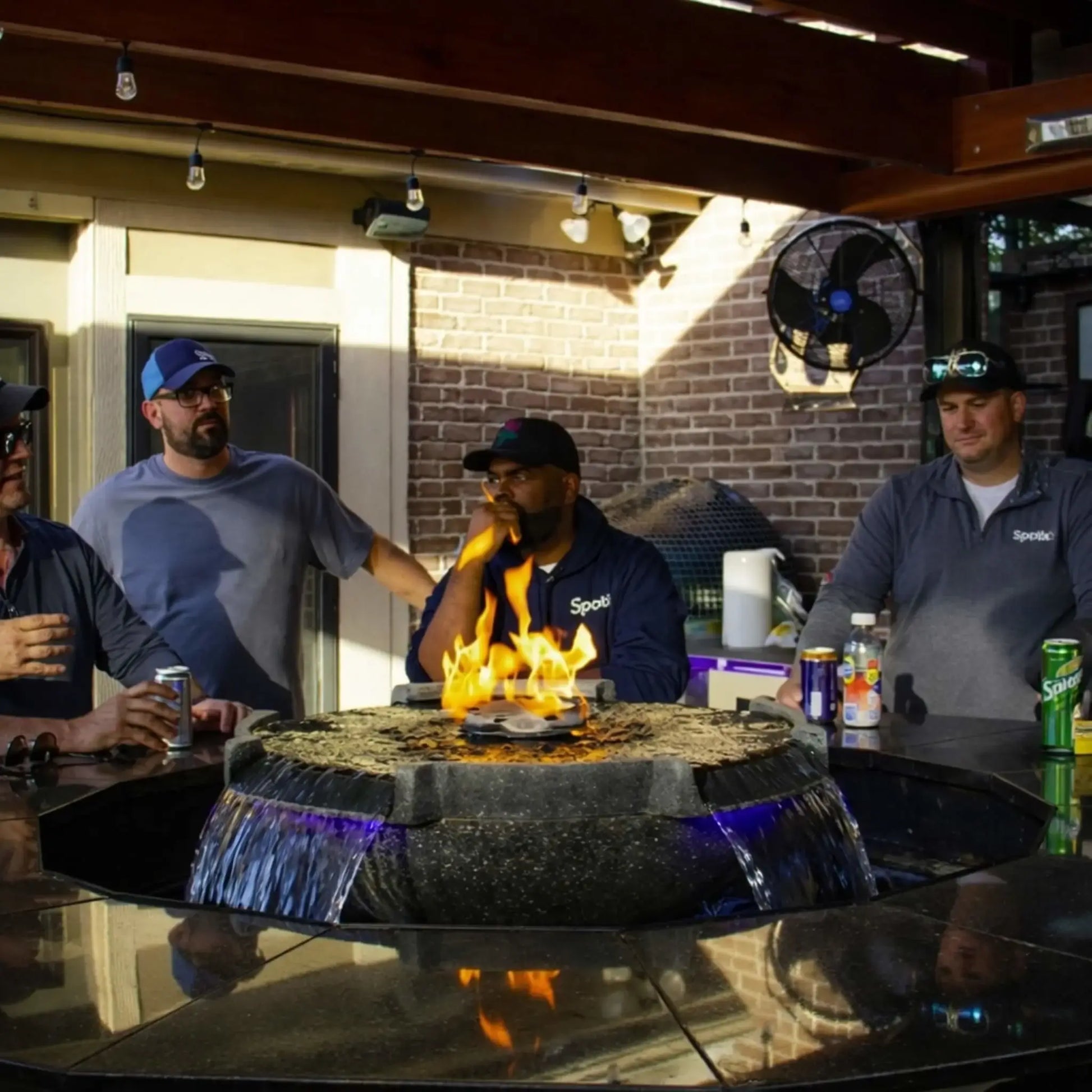 Modern outdoor bar setting featuring HPC Fire Hearth Products H2O n fire fire water feature embedded in a countertop. A group of men gather around the fire and water display, where flames dance above water flow illuminated with subtle lighting, creating a high-end entertainment atmosphere.