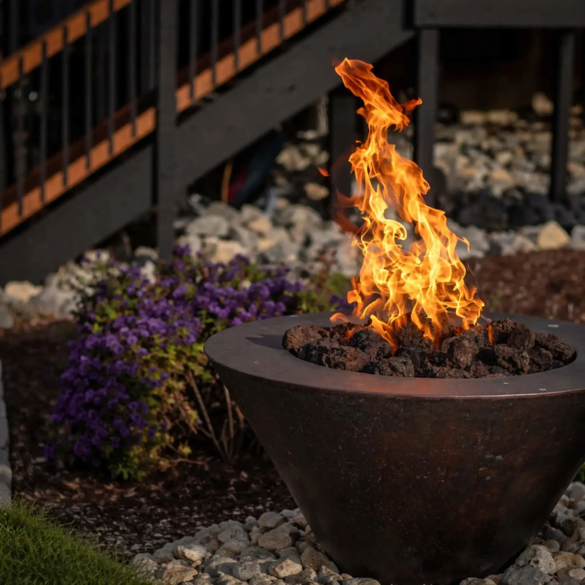 Close-up of a linear gas fire feature with black lava rock and evenly spaced flames, integrated into a concrete fire pit design, emphasizing the burner system and glowing fire pattern behind a glass wind guard.