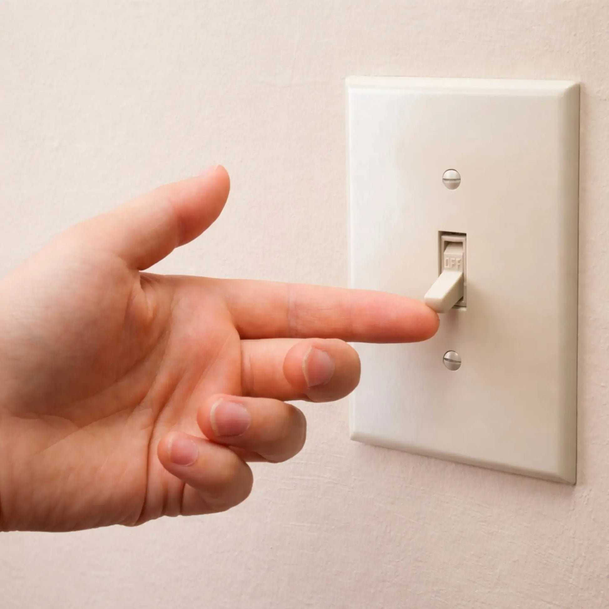 A hand flipping a standard white wall-mounted light switch to the off position. The close-up highlights a simple toggle switch plate against a neutral wall, representing basic on/off electrical control commonly used for lighting or ignition systems.