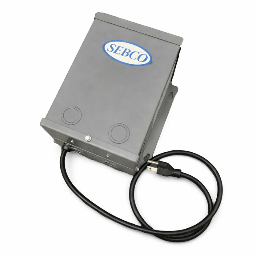 Product image of a SEBCO magnetic transformer housed in a durable gray metal enclosure with a hinged cover and mounting tabs. The unit features a prewired black power cord with a standard plug and knockout ports on the front for electrical connections. Designed for fire pit ignition systems, this low-voltage power supply is suitable for indoor or outdoor use and built for reliable performance in ignition control setups.