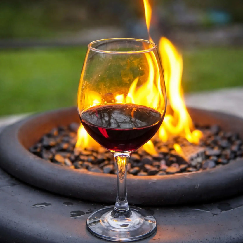 Wine glass filled with red wine placed in front of a lit HPC Portable Sport Pit fire pit. Flames reflect through the glass, creating a warm, inviting atmosphere that showcases the fire pit’s role in relaxing outdoor evenings.