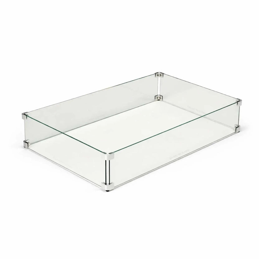 Rectangular tempered glass wind guard for outdoor fire pit tables displayed on a clean white background. The clear glass panels are secured with polished metal corner brackets and supports, designed to shield flames from wind while maintaining a sleek, modern appearance for linear gas fire features.