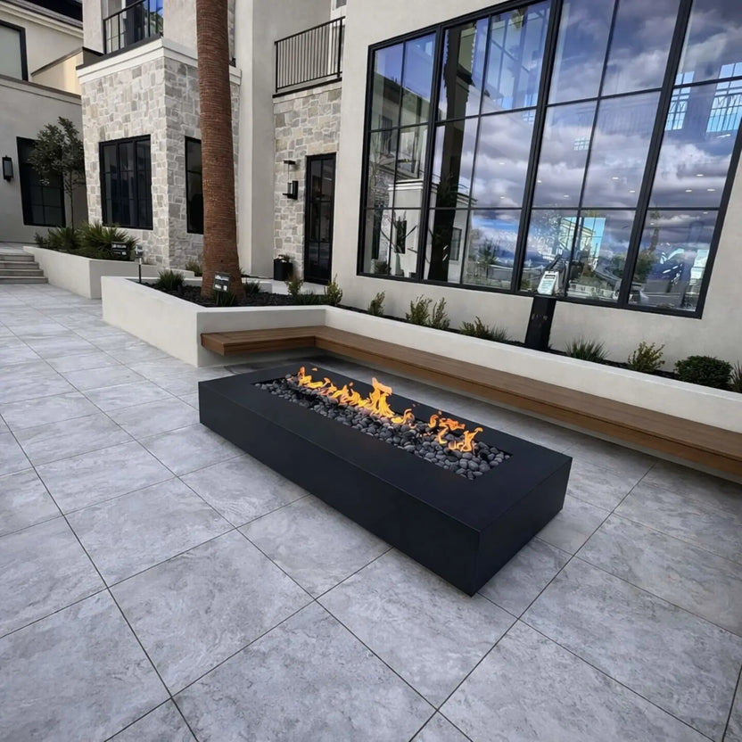 Circular stone fire pit with a metal burner ring and lava rock fill, shown from above with vibrant flames rising. The surrounding patio features curved pavers and outdoor seating, highlighting a functional and visually appealing backyard fire feature.