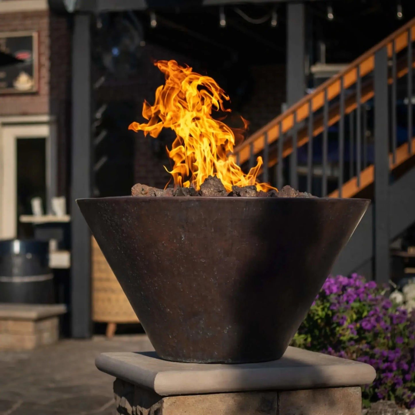 Large backyard patio featuring a central round fire pit surrounded by cushioned seating under a wooden pergola with string lights. A swimming pool with a slide sits in the foreground, creating a luxurious outdoor living space ideal for entertaining.
