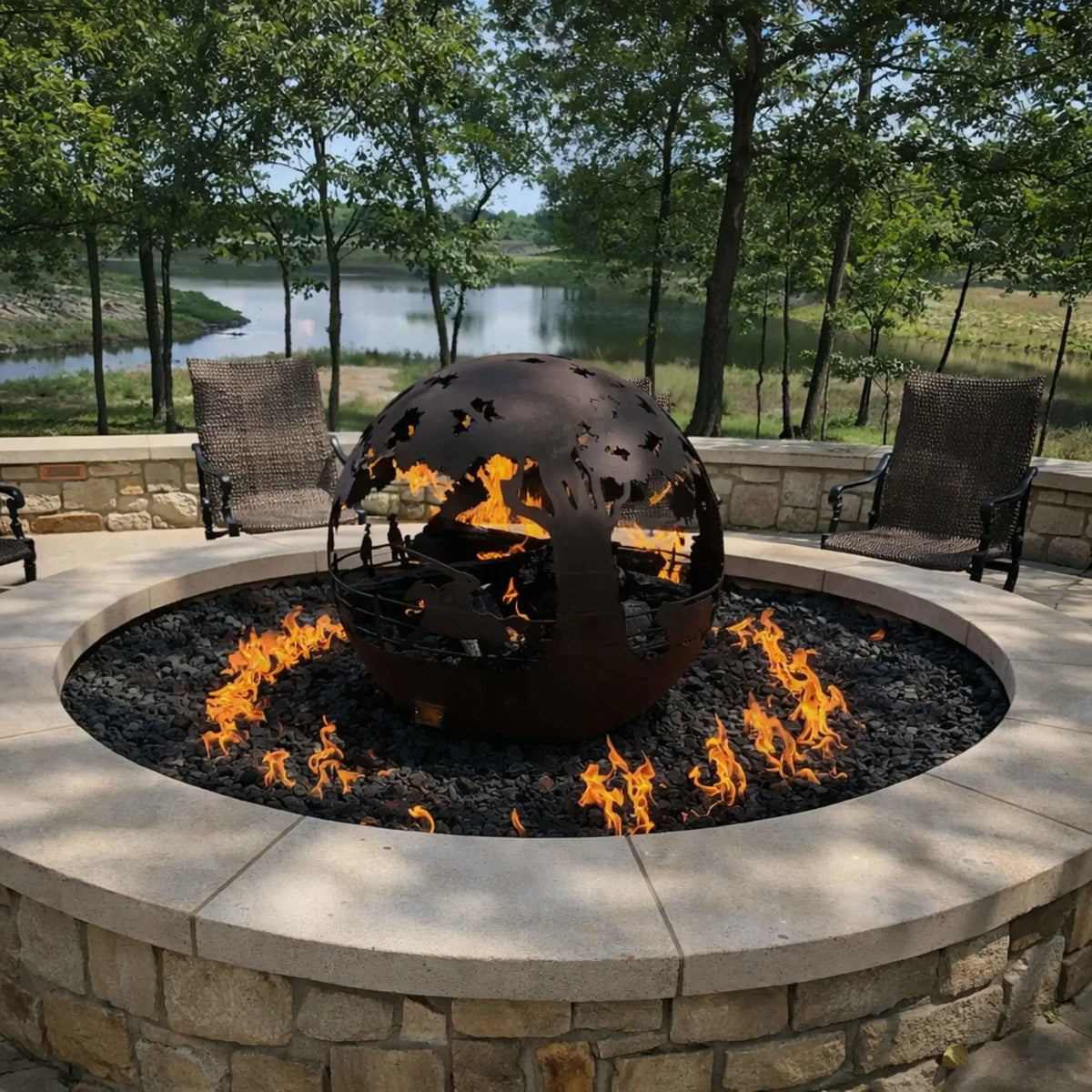 Stone-built circular fire pit with a wide ledge and stacked log fire, placed in a landscaped yard with rolling hills and large trees. The warm flames contrast against the open countryside view, creating a peaceful outdoor retreat.