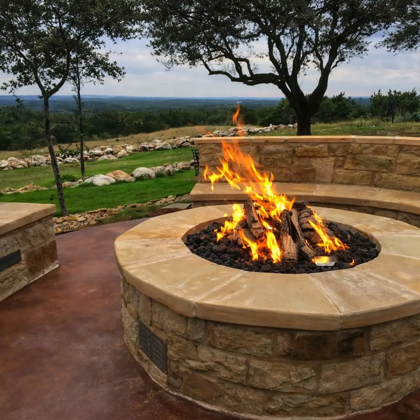 Outdoor stone fire pit with a clean, round design and bright flame display, surrounded by built-in curved seating walls. The setting overlooks a scenic landscape with trees and distant views, offering a comfortable and inviting gathering space.