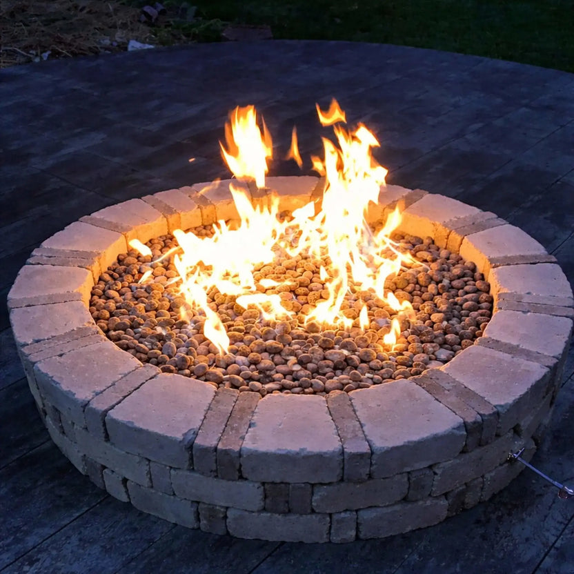 DIY-style circular brick fire pit with stacked stone blocks and lava rock media, showcasing strong natural gas flames on a wooden deck at dusk, emphasizing a simple yet functional backyard fire feature installation.