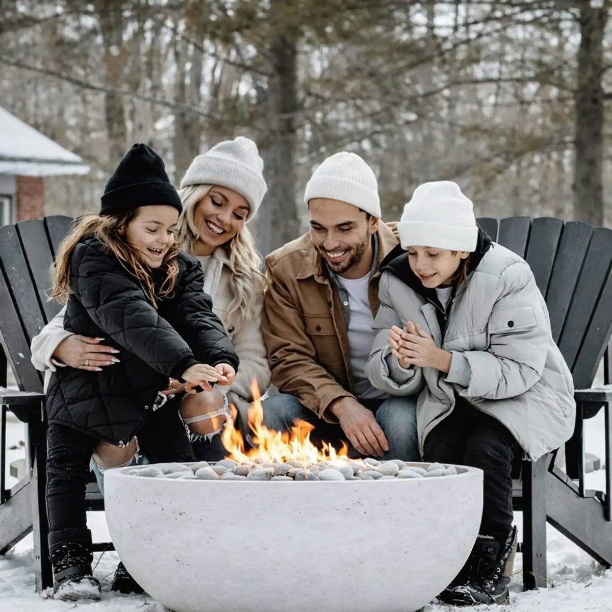 Family of four gathered around a round concrete fire pit in a snowy backyard, wearing winter clothing and warming their hands over the flames, highlighting year-round use of a gas fire pit in cold-weather outdoor living spaces.