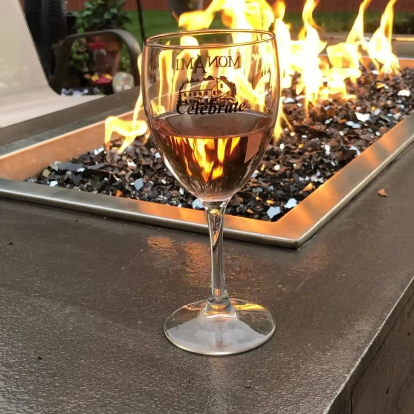 Close-up of a wine glass filled with rosé placed beside a rectangular fire pit burner filled with glossy black fire glass, reflecting flickering flames and creating a warm, intimate outdoor ambiance.