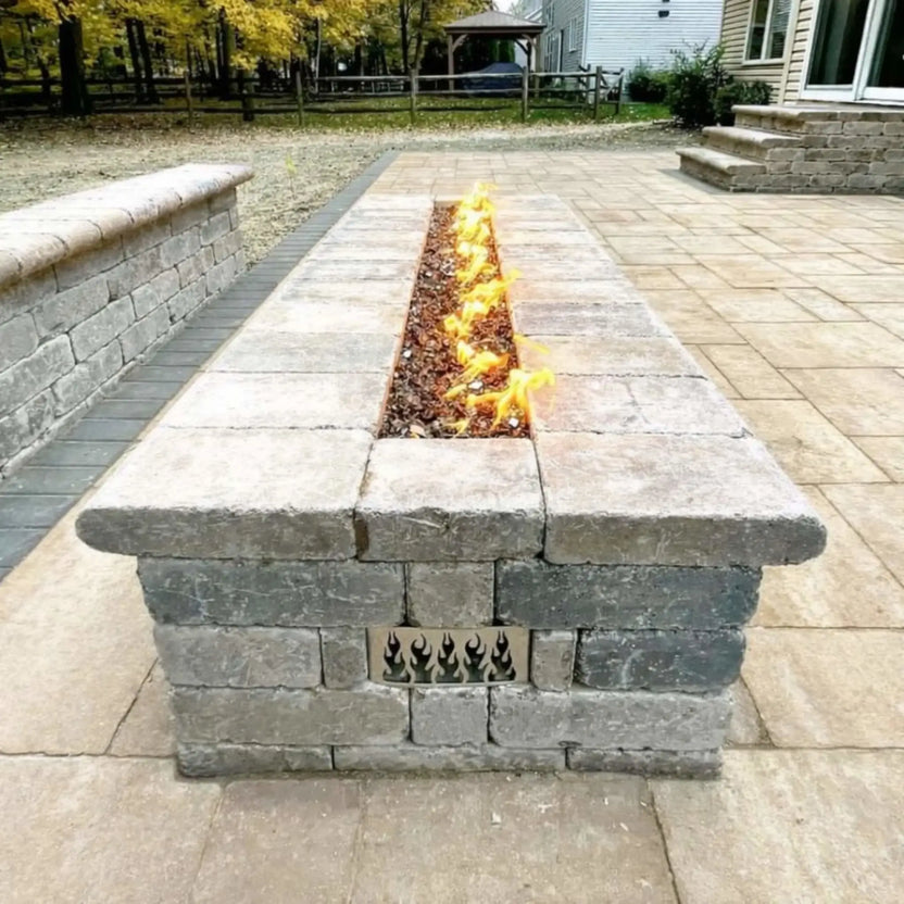 Residential backyard paver patio with a built-in linear fire pit using HPC Fire Hearth Products Torpedo Linear Interlink Pan and T Burner, showcasing warm flame output, integrated seating wall, and clean rectangular fire feature design.