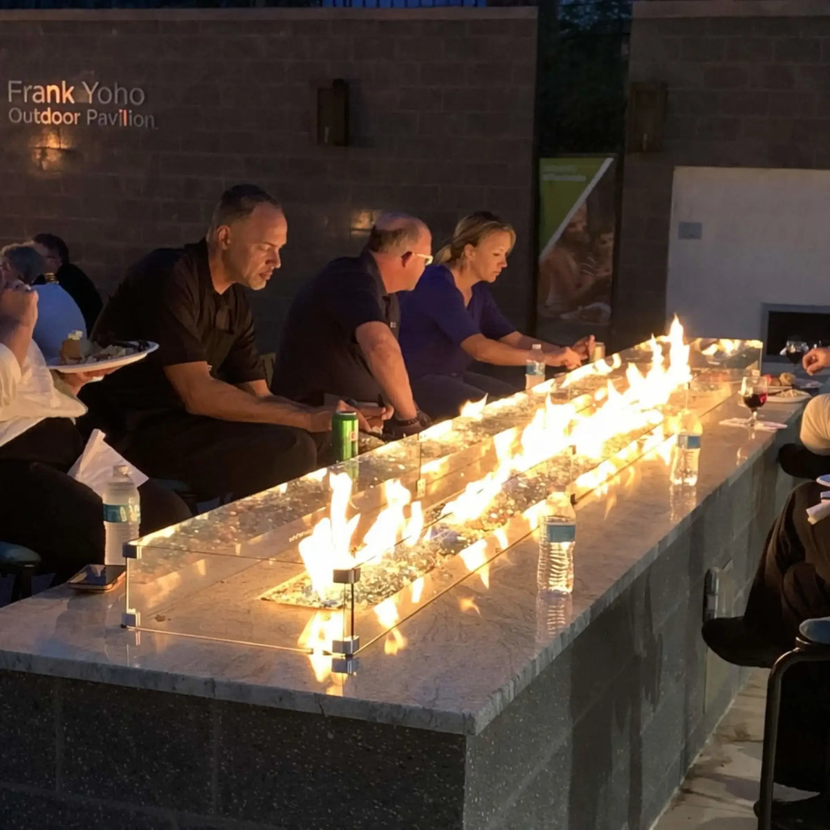 Elegant outdoor gathering space with a long granite fire table powered by HPC Fire Hearth Products Torpedo Linear Interlink Pan and T Burner, featuring glass wind guard, linear flames, and modern seating arrangement for entertaining.