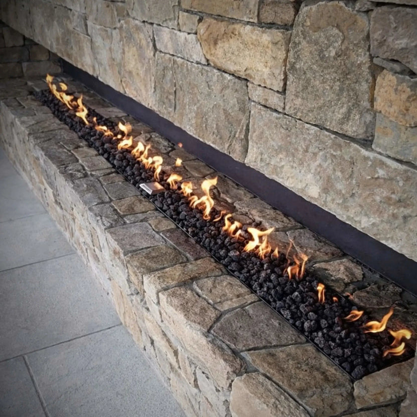 Evening social setting around a large linear fire feature using HPC Fire Hearth Products Torpedo Linear burner system, showcasing bright flames, glass wind guard, and guests enjoying the warmth in a premium outdoor pavilion.