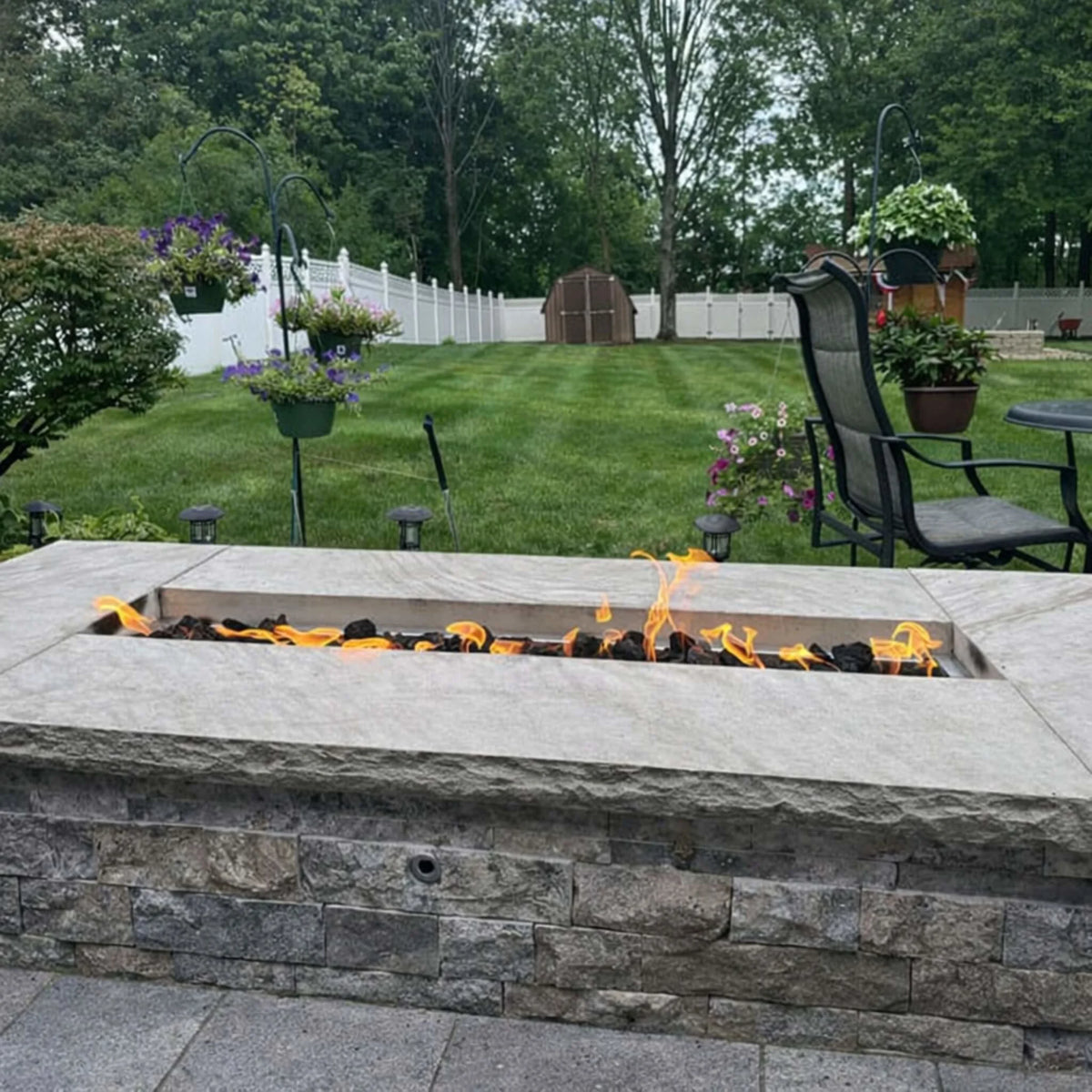 Backyard stone fire feature with a long linear burner producing a soft, low Lo flame across lava rock media. The subtle flame height emphasizes the Hi/Lo functionality of the HPC Torpedo system, allowing precise control through electronic ignition systems.