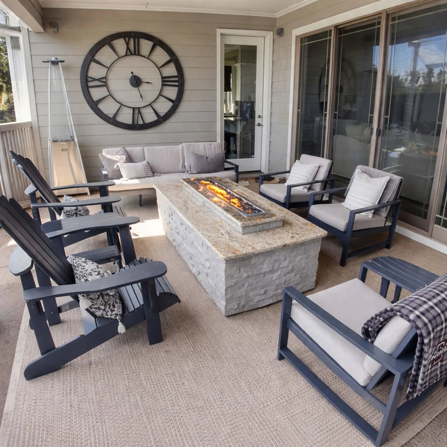Covered patio seating area with a rectangular stone fire table using an HPC Torpedo linear burner. Flames burn steadily at a medium setting, creating a warm focal point while showcasing adjustable Hi/Lo flame control for comfort and ambiance.