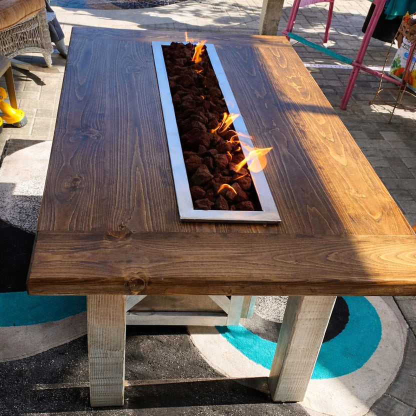 Rustic wooden fire table showcasing an HPC Torpedo linear burner with lava rock media burning at a lower Lo flame setting. The image highlights subtle ambiance and the system’s precise Hi/Lo control capabilities using remote or app-based ignition.