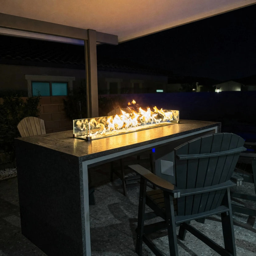 Nighttime outdoor bar setting featuring the HPC Torpedo Linear Trough Pan and T Burner enclosed in glass wind guards, installed in a granite countertop, creating a clean, modern fire display for entertaining spaces.