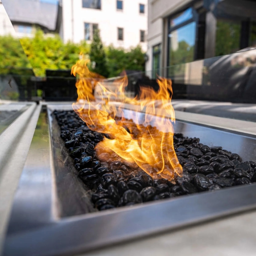 Close-up of the HPC Torpedo Linear Trough Pan and T Burner with black fire glass, highlighting detailed flame movement and the stainless steel burner edges in a modern outdoor patio setting.