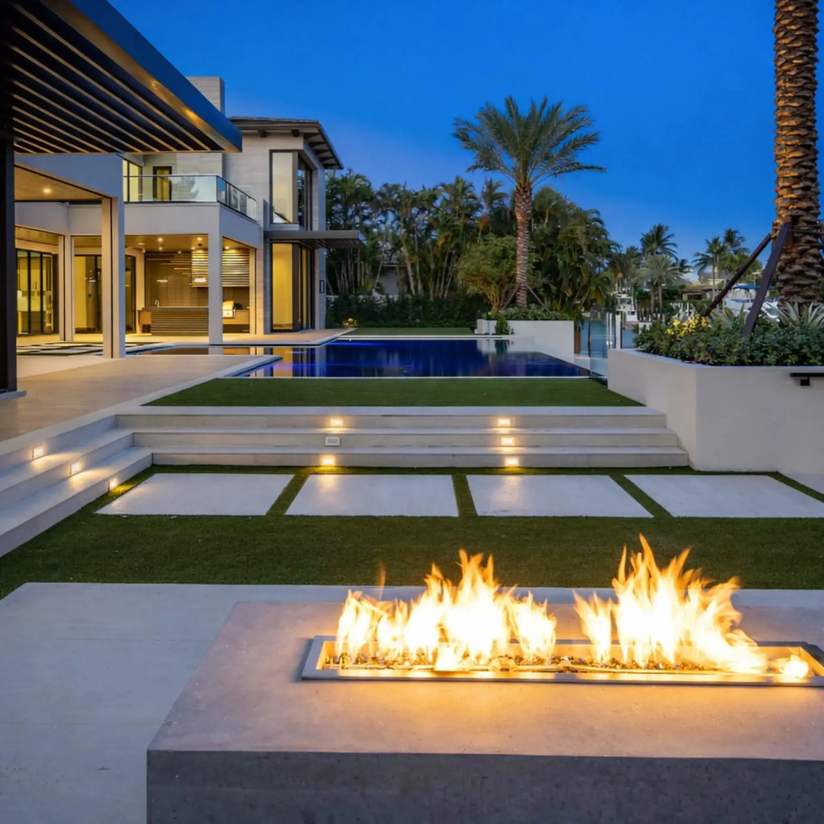 HPC Fire Hearth Products Controls torpedo linear trough burner integrated into a luxury outdoor fire feature near a modern home and pool. The high capacity match lit ignition system produces vibrant linear flames, enhancing the sleek architectural design of this upscale backyard living space.
