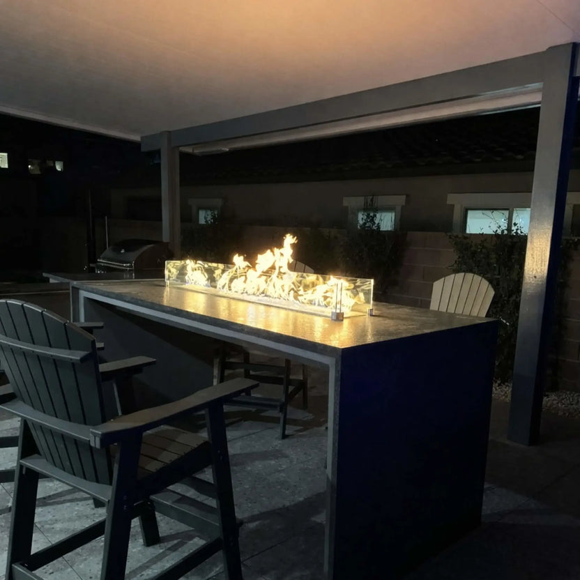 Outdoor covered bar area featuring a sleek fire table with glass wind guard, powered by the HPC Fire Hearth Products Torpedo Linear Trough Pan and T Burner Match Lit CSA MLFPK FLEX burner system. The continuous flame line demonstrates efficient gas flow and dependable ignition. This CSA match lit fire feature emphasizes ease of use, clean design, and consistent performance for entertaining environments.