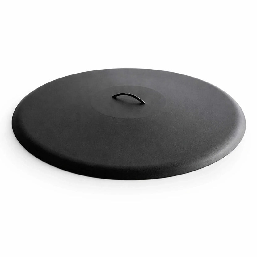 Low-profile round aluminum fire pit burner cover in a matte black finish, featuring a smooth, slightly domed surface with a subtle textured coating. A centered curved metal handle sits flush within a recessed top section for easy lifting. The clean white background highlights the minimalist design, durable construction, and modern aesthetic ideal for protecting outdoor fire pit burners.